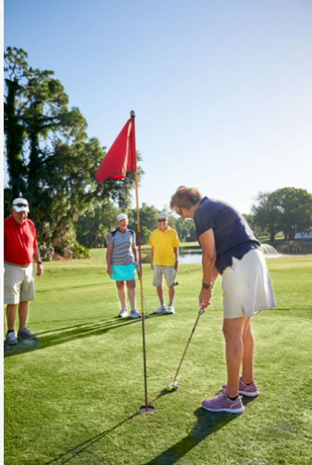 A senior woman putts on a golfing green.