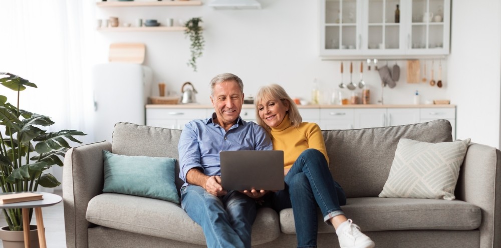 Senior couple sitting on a couch while using laptop