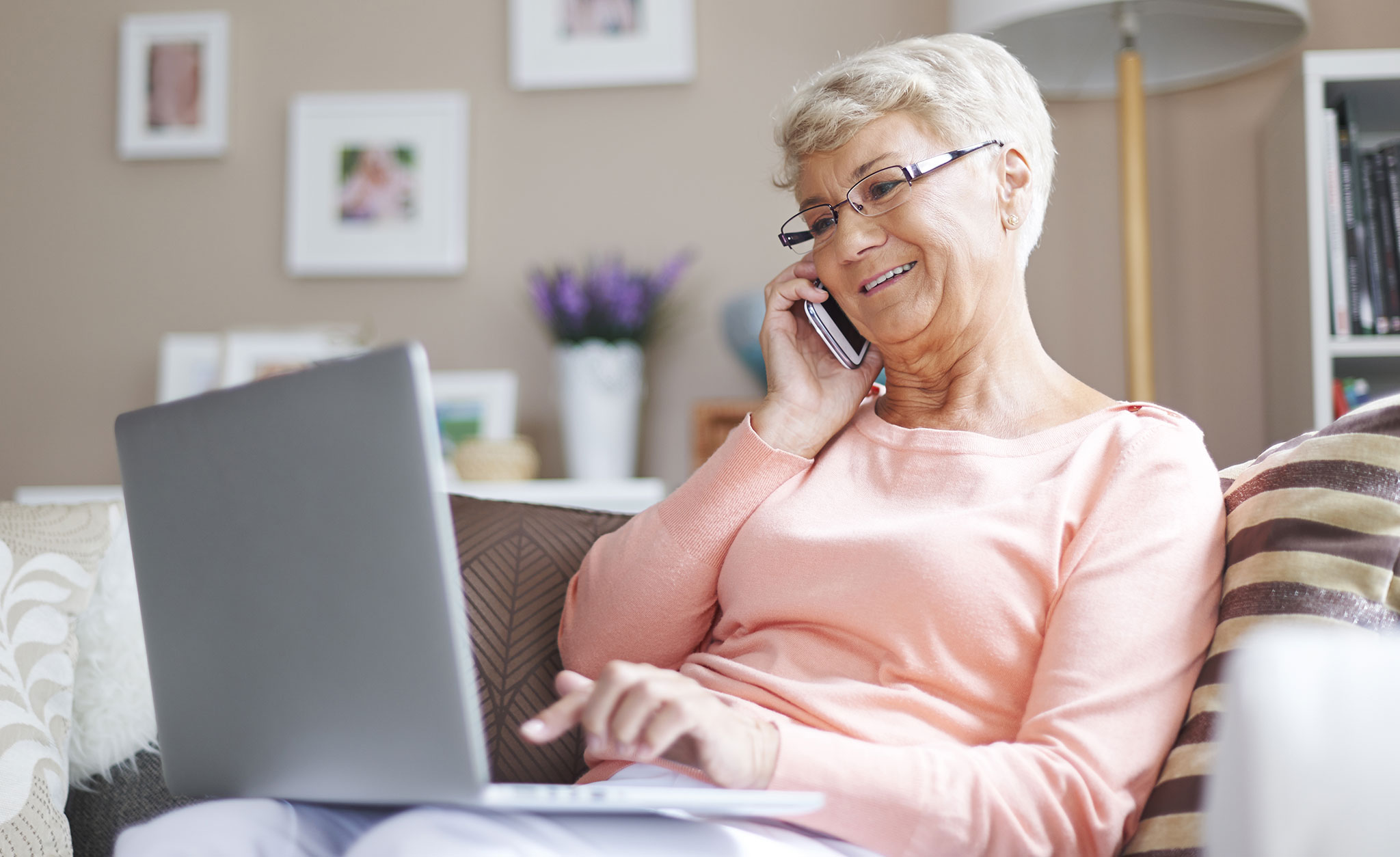 A senior woman talks on her cell phone while working on a laptop.