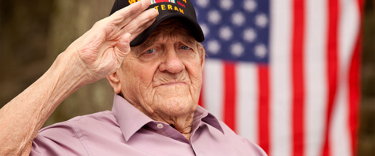 Senior citizen military veteran saluting in front of an American flag