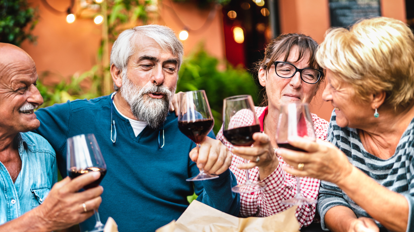 Group of four older adults smiling and toasting with glasses of red wine