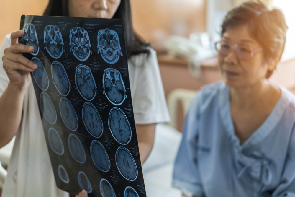 a senior woman in a hospital gown listens while a doctor shows her the MRI scans of her brain