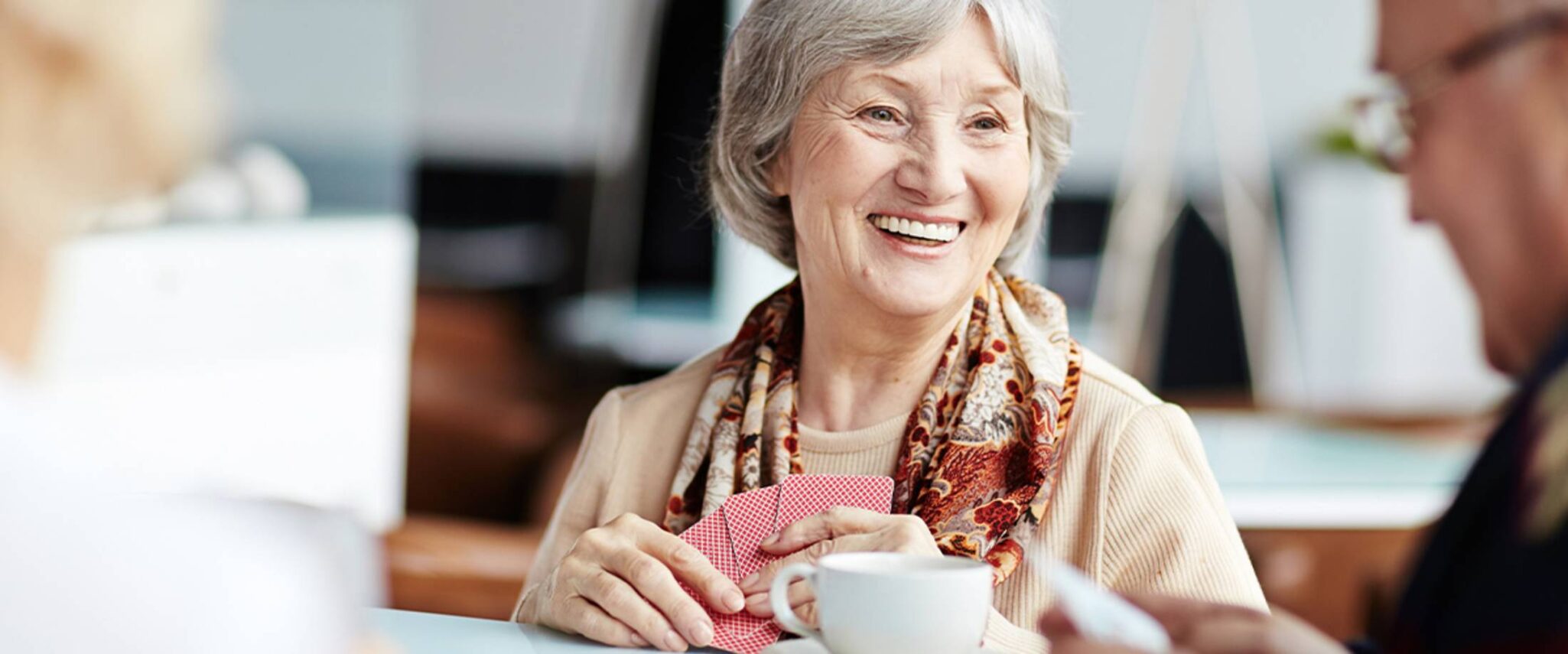 elderly woman playing cards with senior friends drinking coffee
