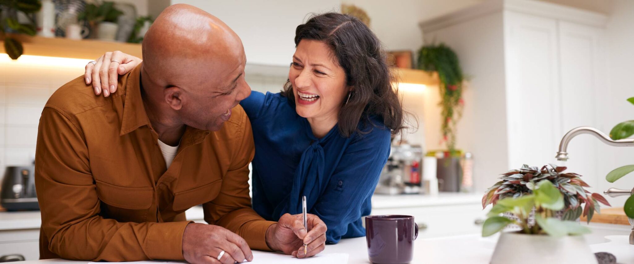 young couple laughing while writing on paper in a kitchen