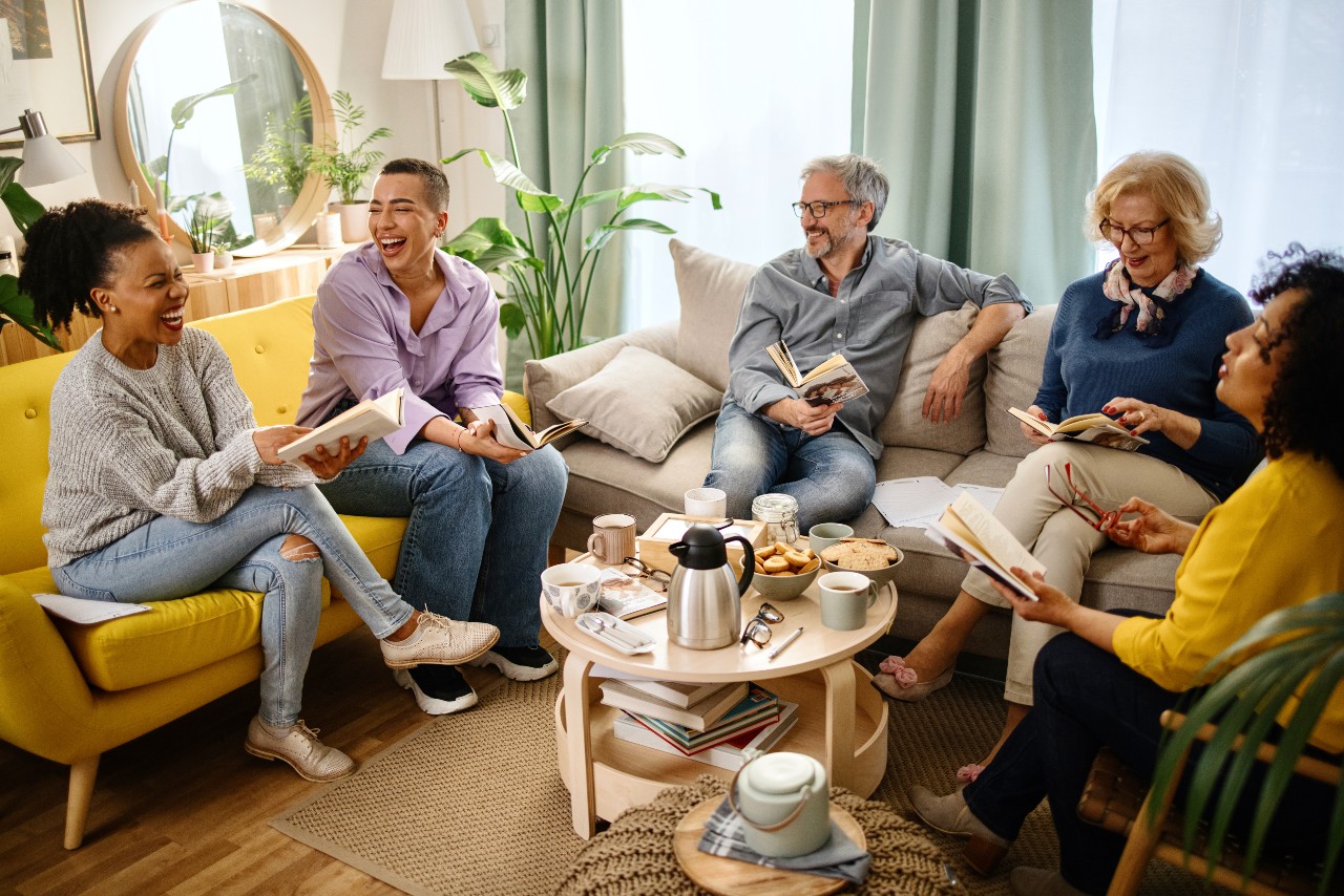 A group of adults come together in a living room for a book club meeting