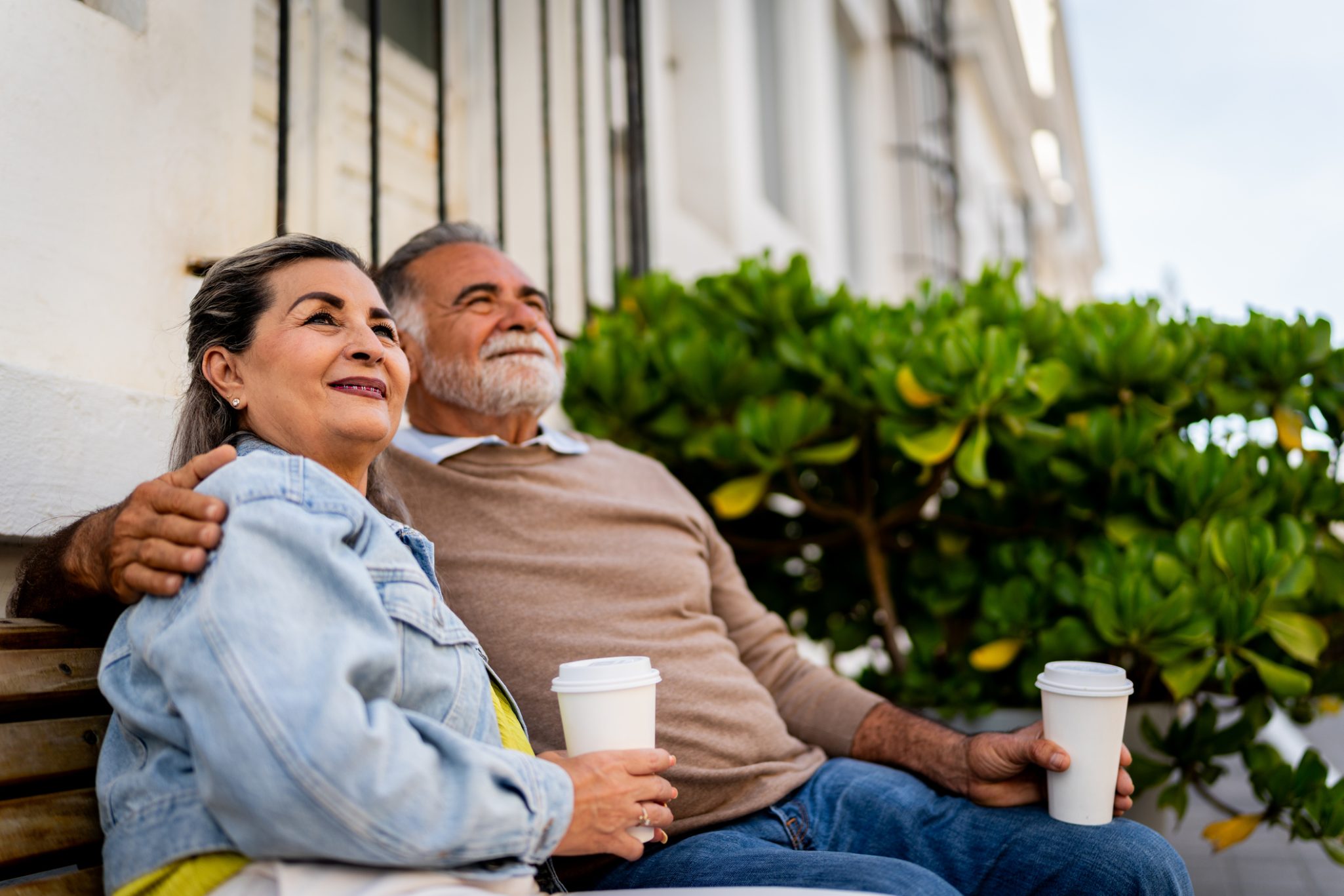 Senior couple sitting on park bench holding cups of coffee